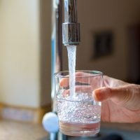 person filling up glass of water from tap